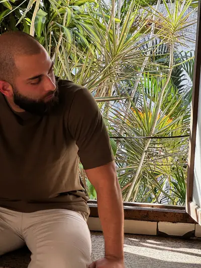 Sentado junto a la ventana con la luz de la tarde, polera marrón UEBOS